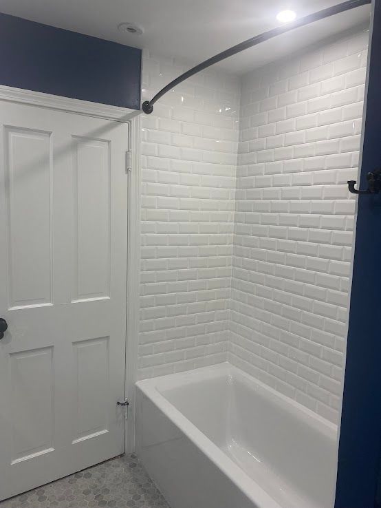 A bathroom featuring a white bathtub, white subway tile wall, and a curved black shower rod against navy blue trim.