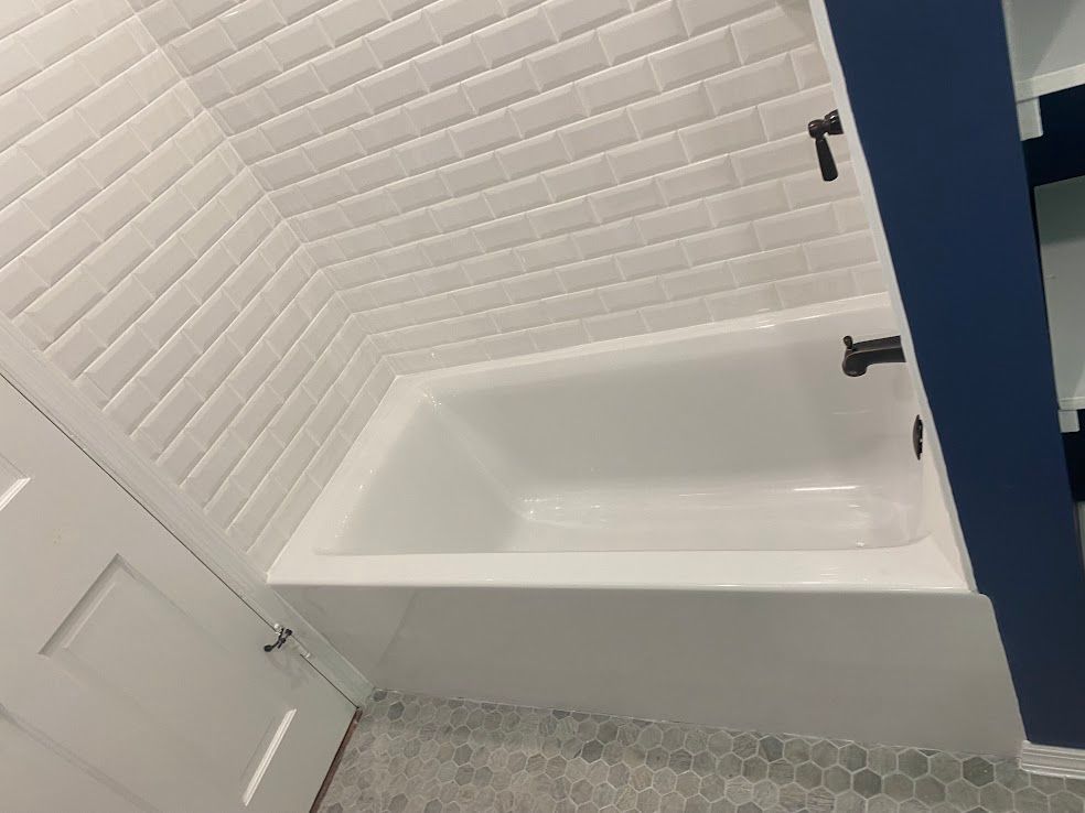 A white bathtub with dark fixtures set against a white subway tile wall and a blue-painted corner wall.