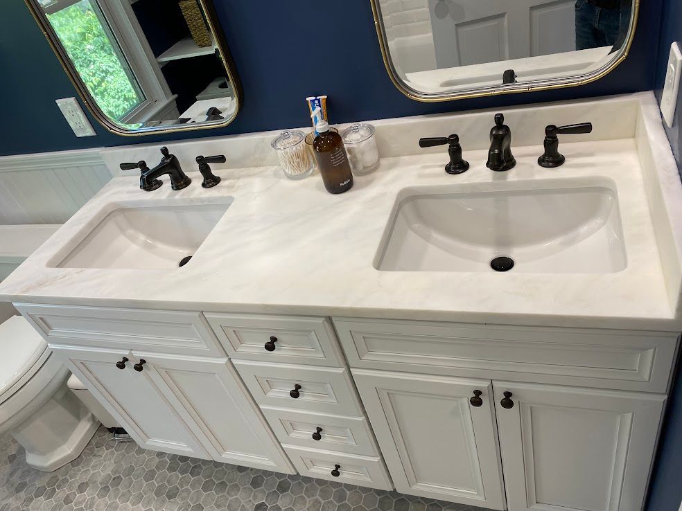 A white double-sink bathroom vanity with dark bronze faucets, marble countertop, and navy blue walls.