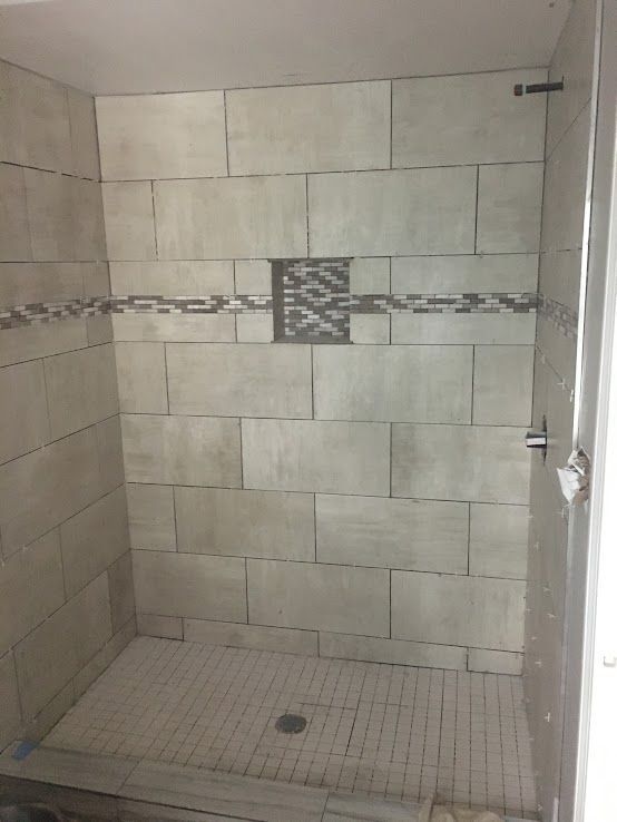 A tiled walk-in shower with large beige wall tiles, a decorative mosaic horizontal band, a recessed niche, and floor tiles.