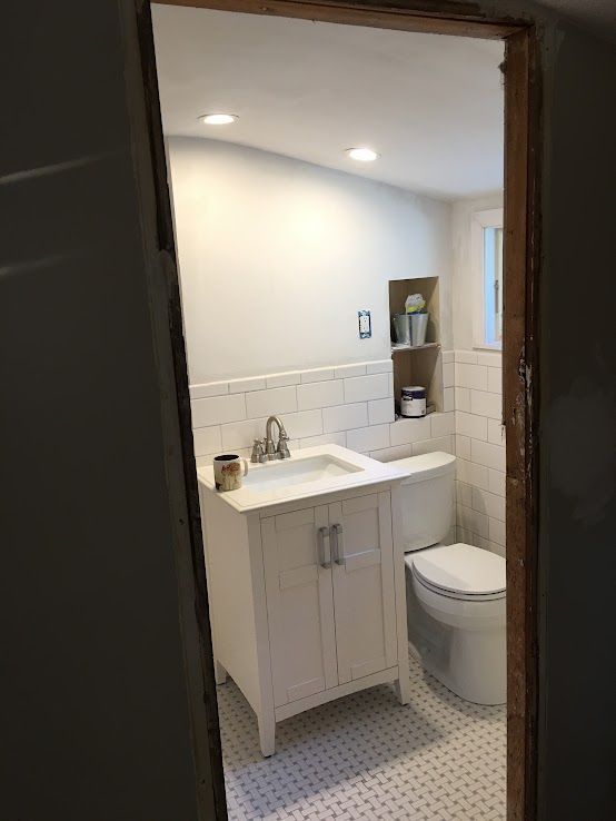A bathroom interior featuring a white vanity with a sink, a toilet, tiled walls, and a recessed wall shelf.
