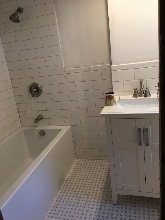 A white bathroom featuring a tub-shower combo with white subway tile walls, a white vanity, and patterned tile flooring.