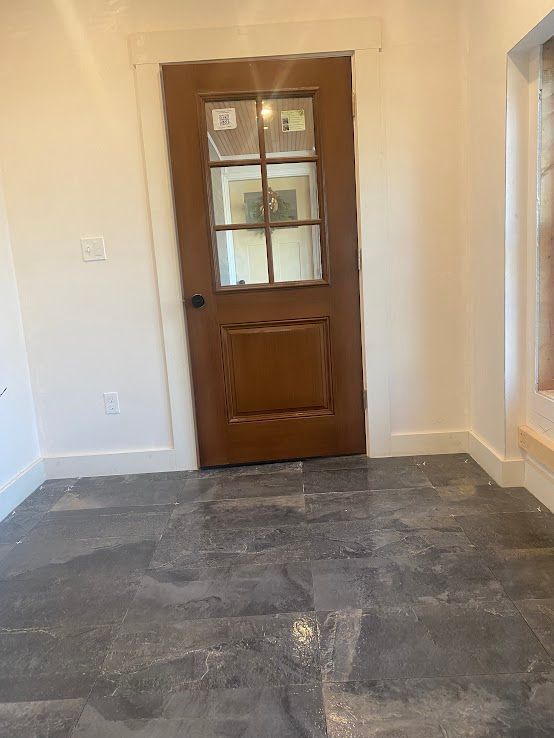 A wooden, six-paneled glass door set in a white frame, centered in a room with dark gray stone-style floor tiles.