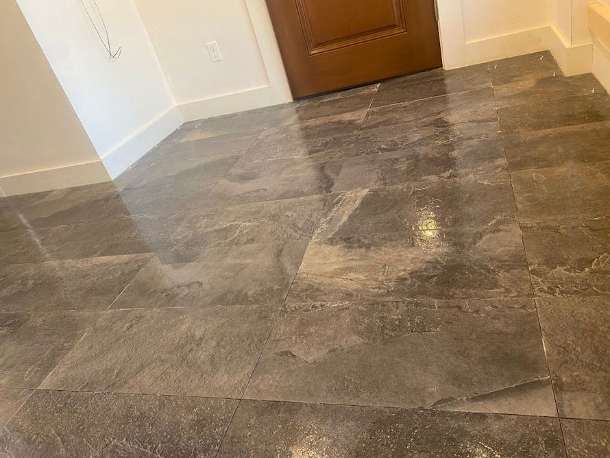 A view of a polished, dark gray stone-tiled floor leading toward a closed wooden door in a room with white walls.