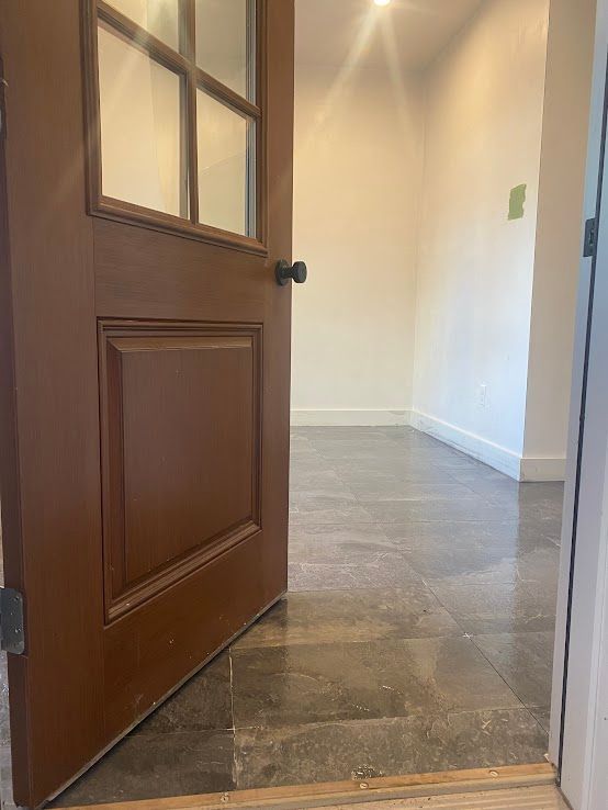 A wooden door with glass panels sits slightly ajar, opening into a room with light walls and grey tile flooring.