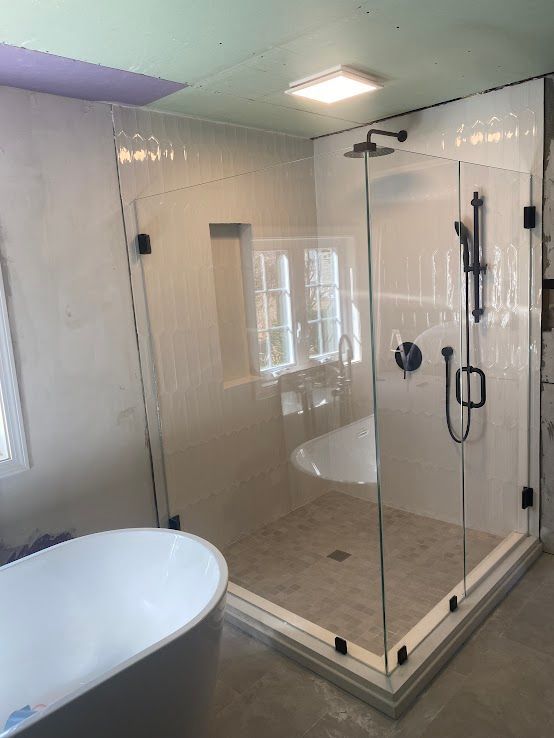 A glass-enclosed shower with matte black fixtures and a built-in shelf, situated next to a freestanding white bathtub.