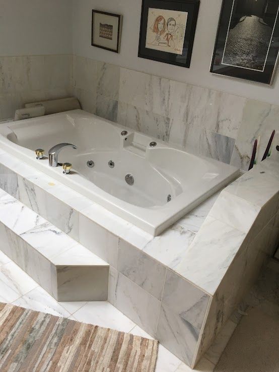 A white jetted bathtub built into a marble platform, featuring a small step and three framed artworks on the wall above.