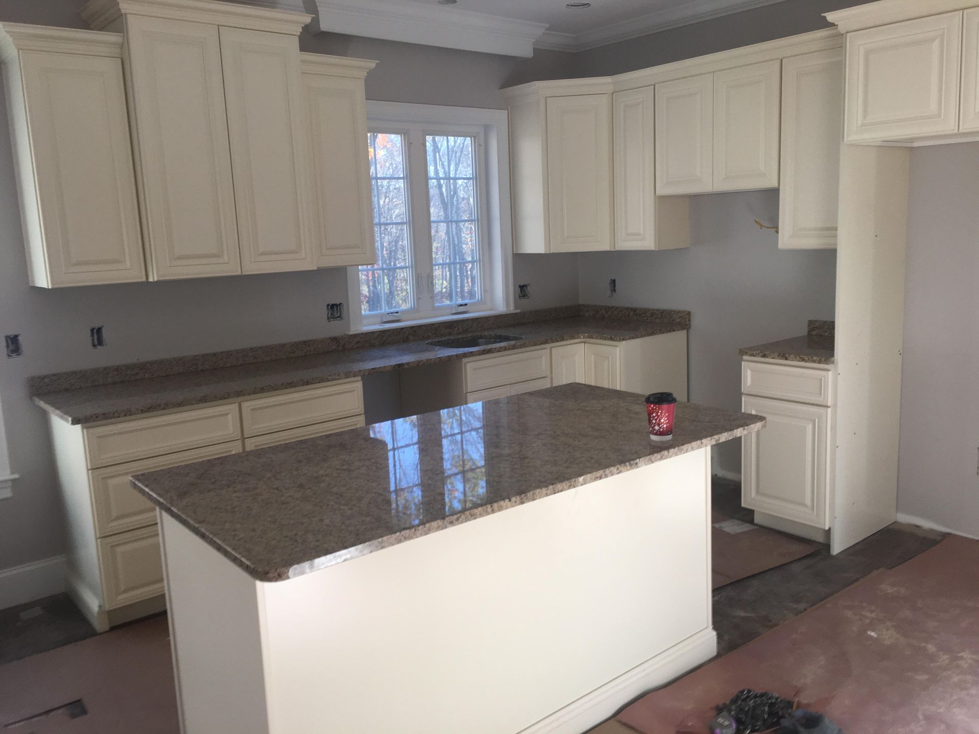 A kitchen under renovation featuring off-white cabinets, granite countertops, and an island in a light gray room.