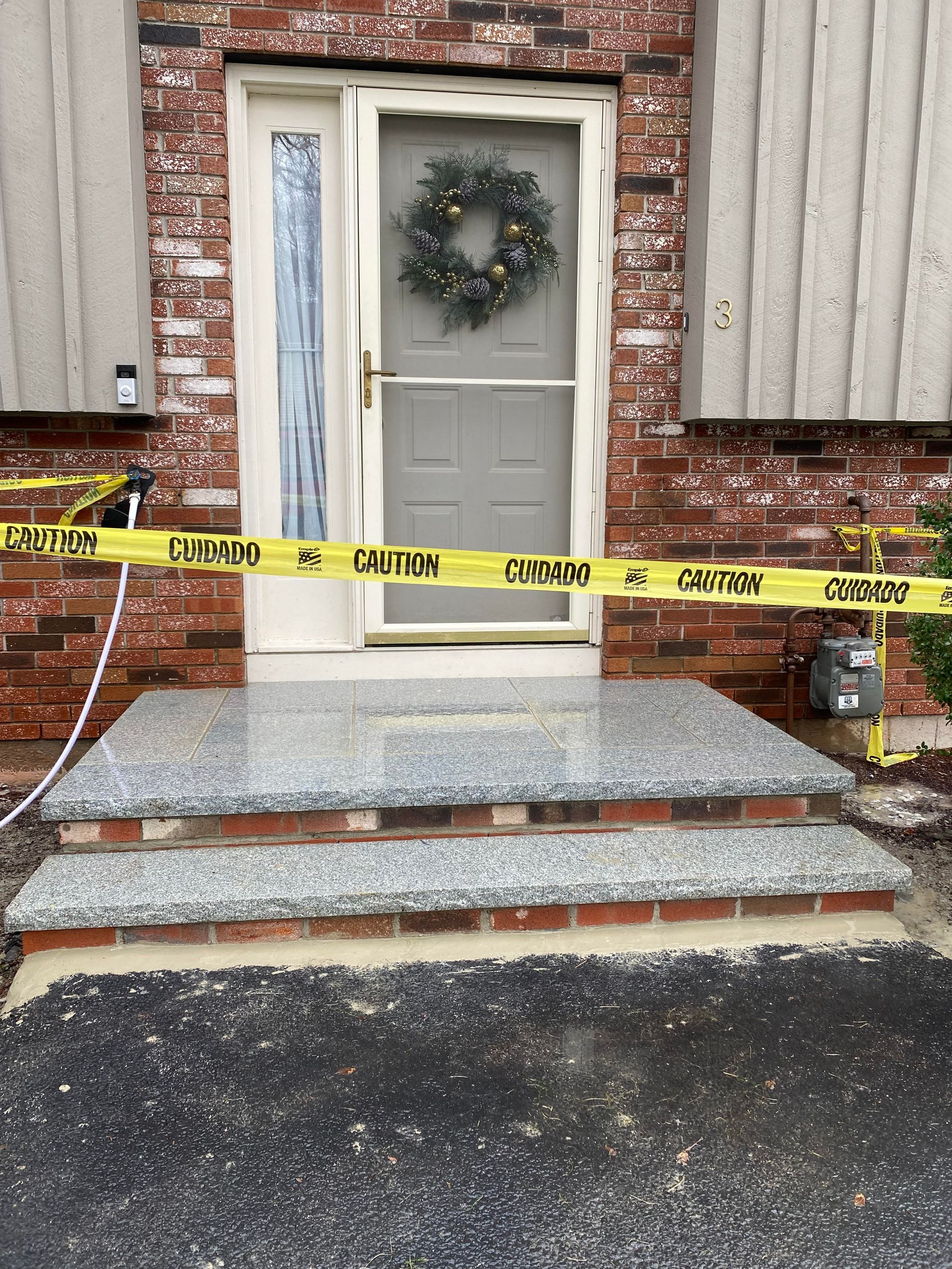 Front steps of a brick house with new gray granite treads and a yellow caution tape strung across the doorway.