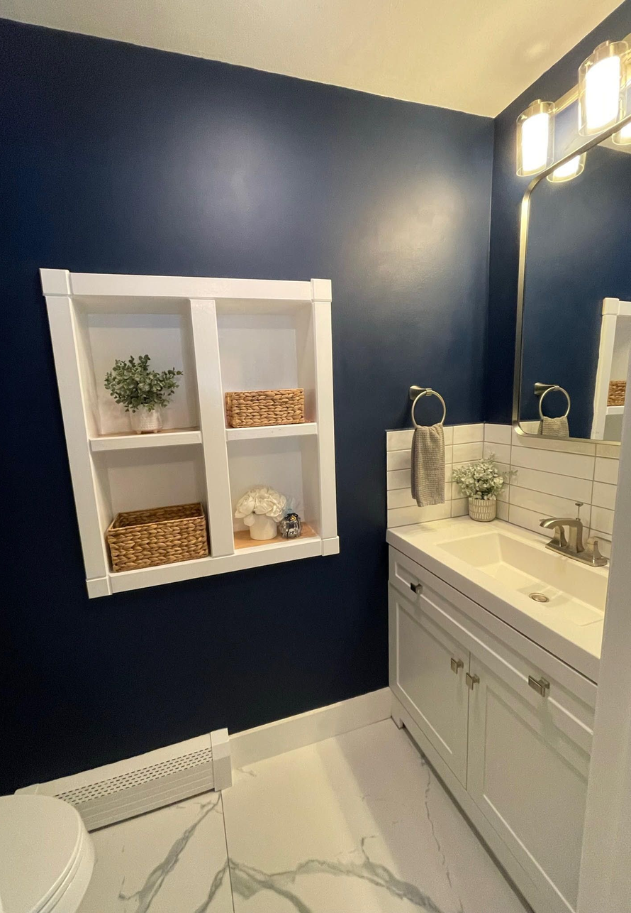 A bathroom featuring dark blue walls, a white built-in shelving unit, a white vanity with a sink, and a light-colored floor.
