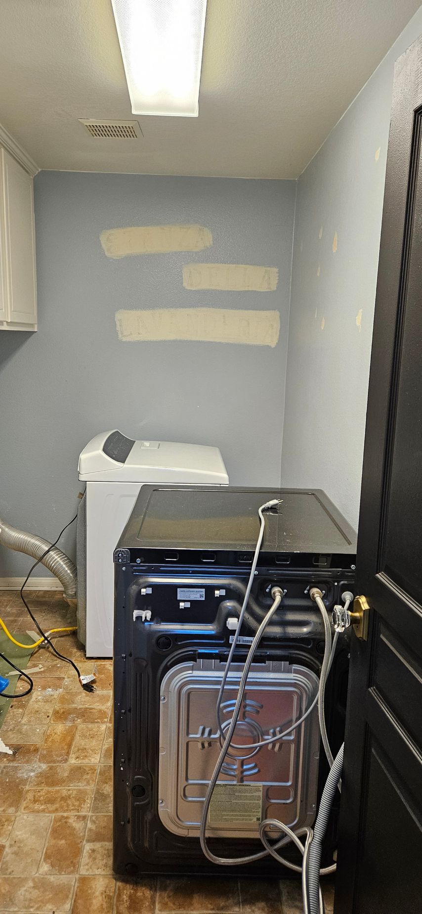 Laundry room with washing machine, dryer, and paint swatches on the wall. Brown tile floor.