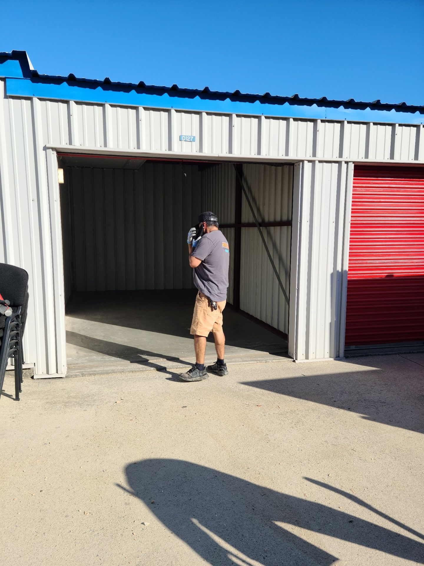 Man standing in the doorway of a storage unit. White and red metal buildings under a blue sky.