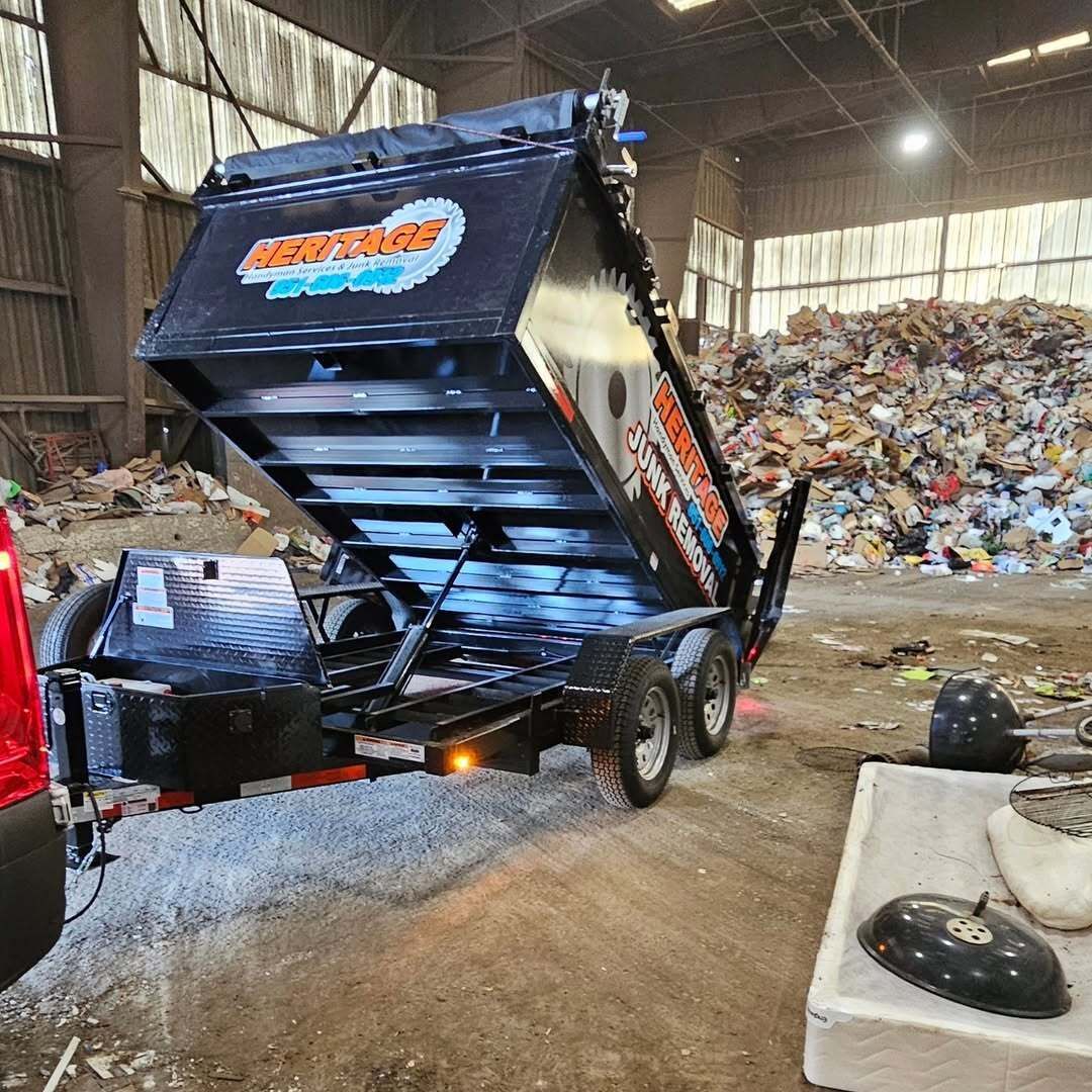 A black dump trailer unloading gravel inside a building, a pile of scrap metal in the background.