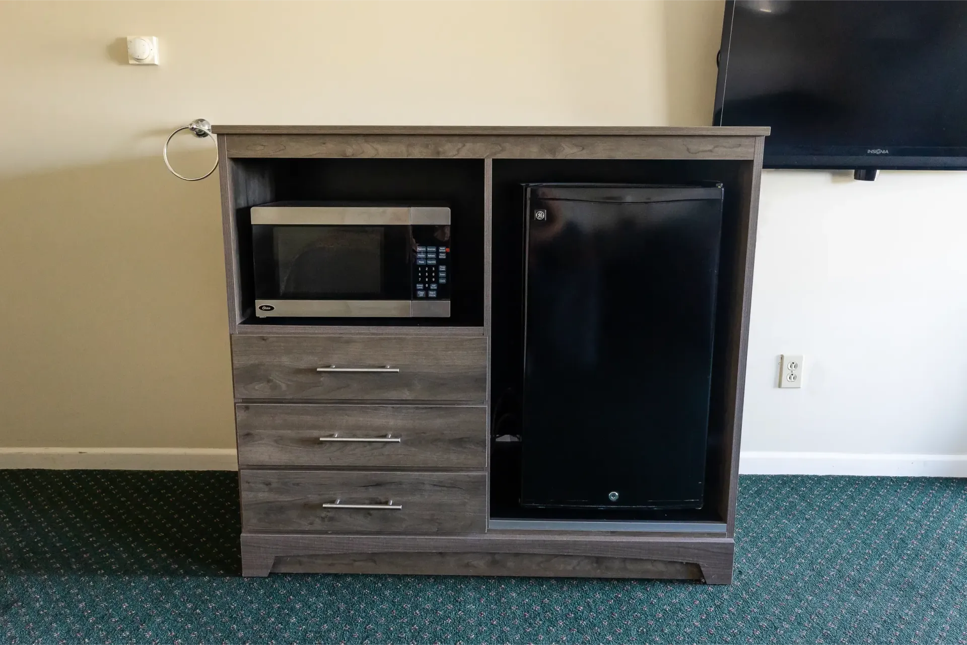 A microwave and refrigerator are on a dresser in a hotel room.