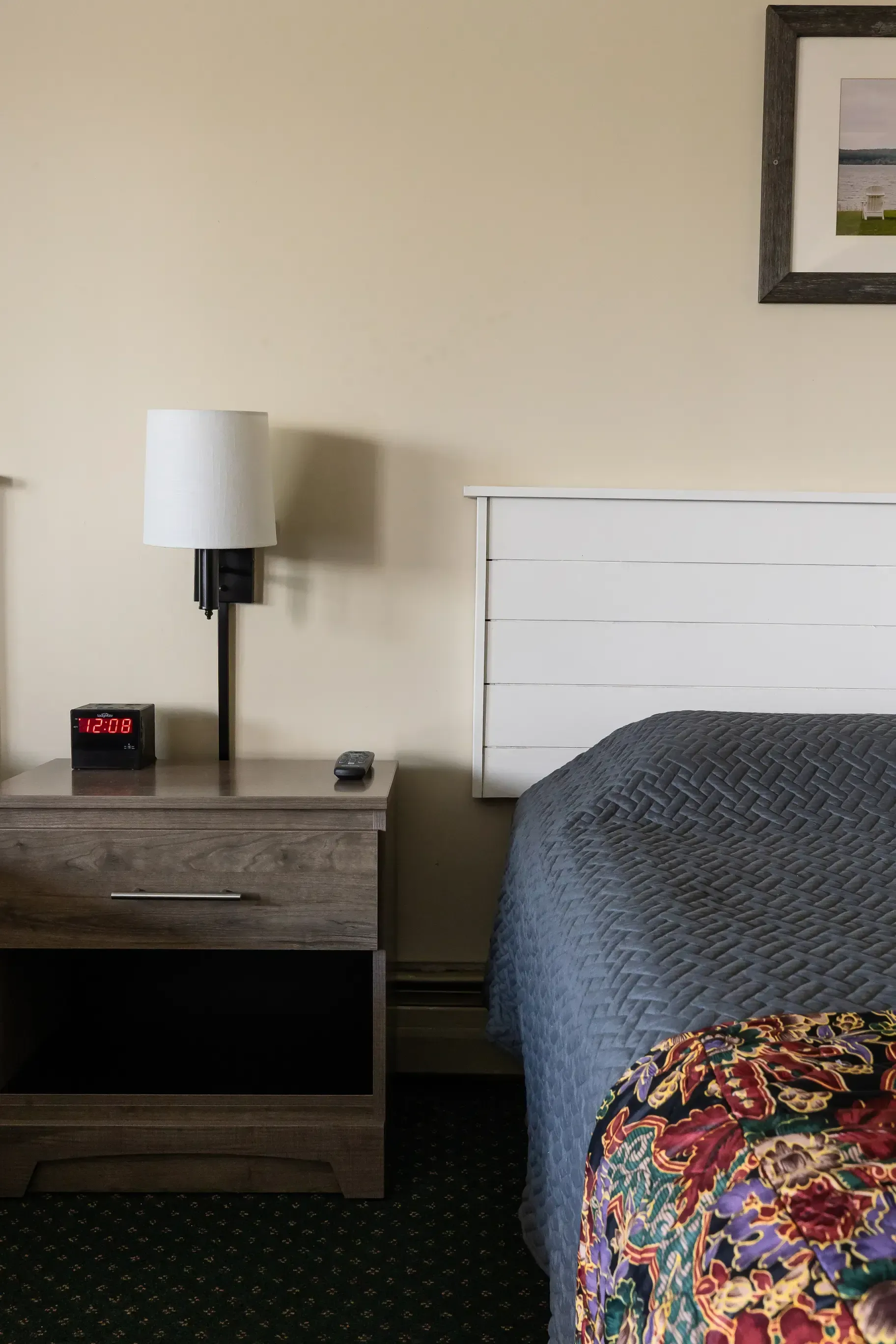A hotel room with a bed , nightstand , lamp and alarm clock