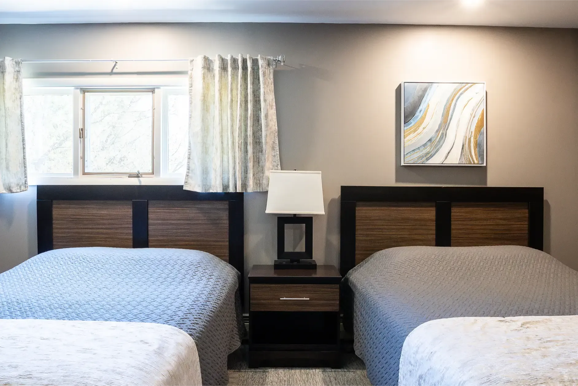 A bedroom with two beds , a nightstand , a lamp and a window.