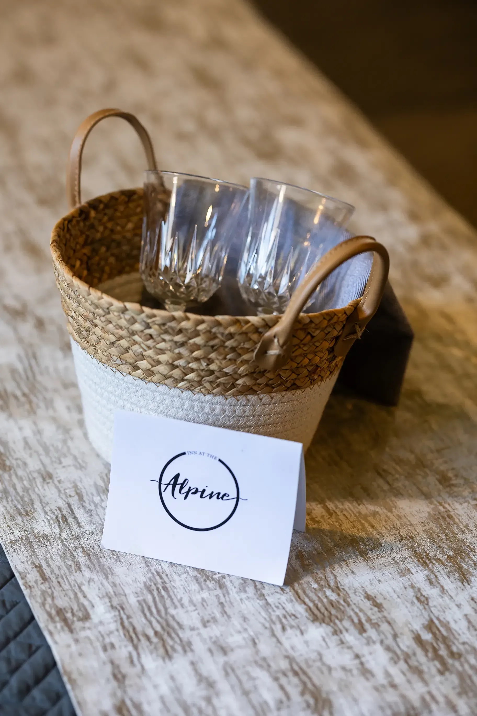 A basket filled with wine glasses and a card on a table.