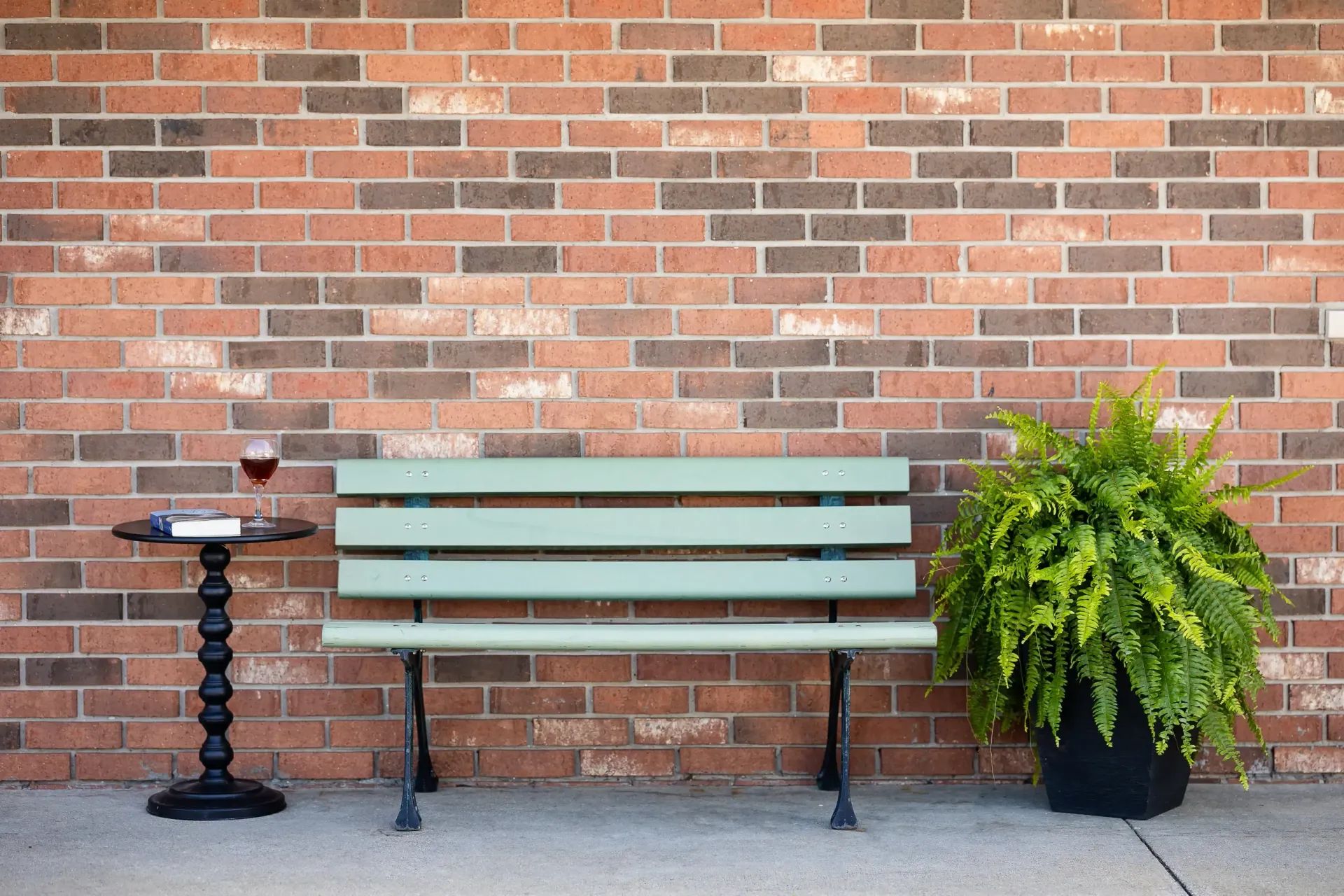 A green bench is sitting in front of a brick wall.