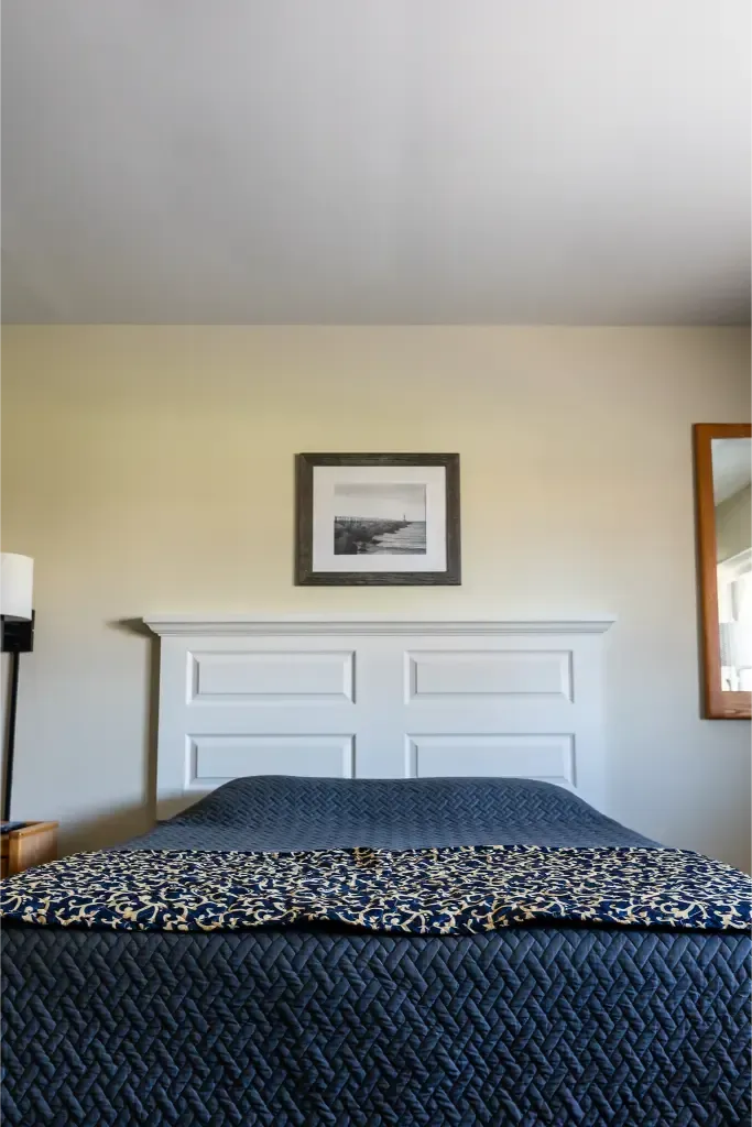 A bedroom with a bed , lamp , mirror and picture on the wall.
