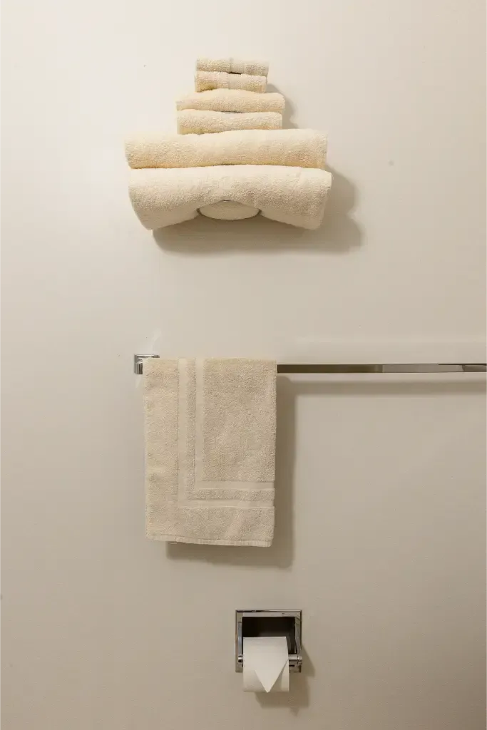 A stack of towels is hanging on a towel rack next to a toilet paper dispenser.