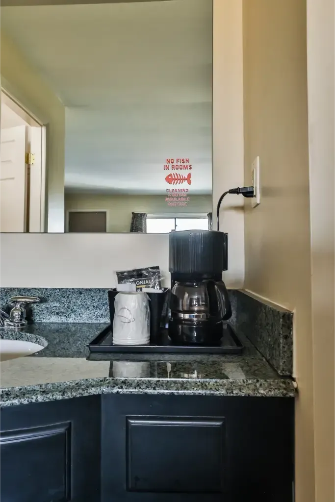 A bathroom counter with a coffee maker and a mirror