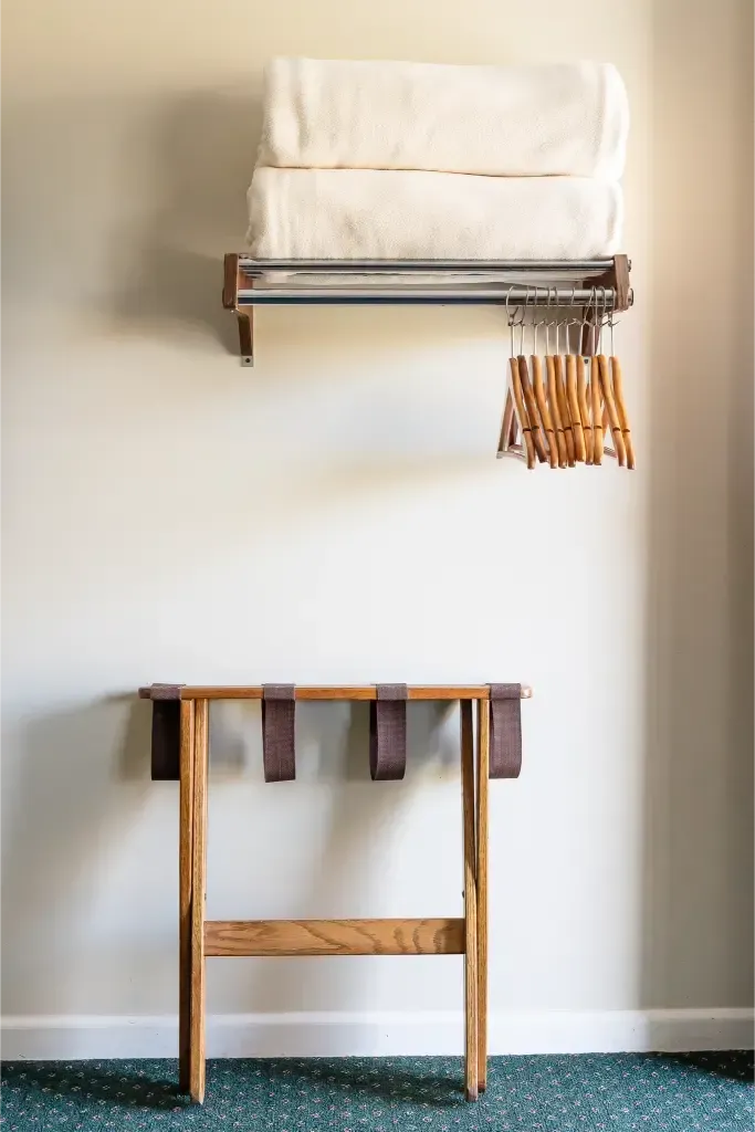 A hotel room with a wooden table and a shelf with towels and clothes hanging on it.