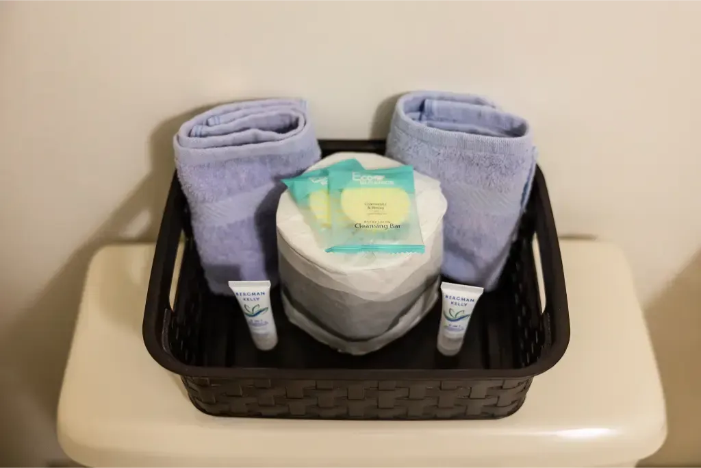 A basket with towels , soap , and toilet paper on a toilet.