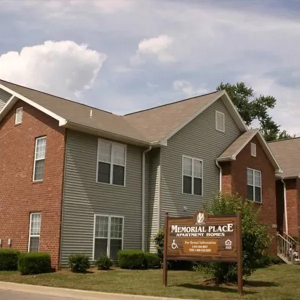 A two-story brick and grey-sided apartment complex with a brown sign labeled