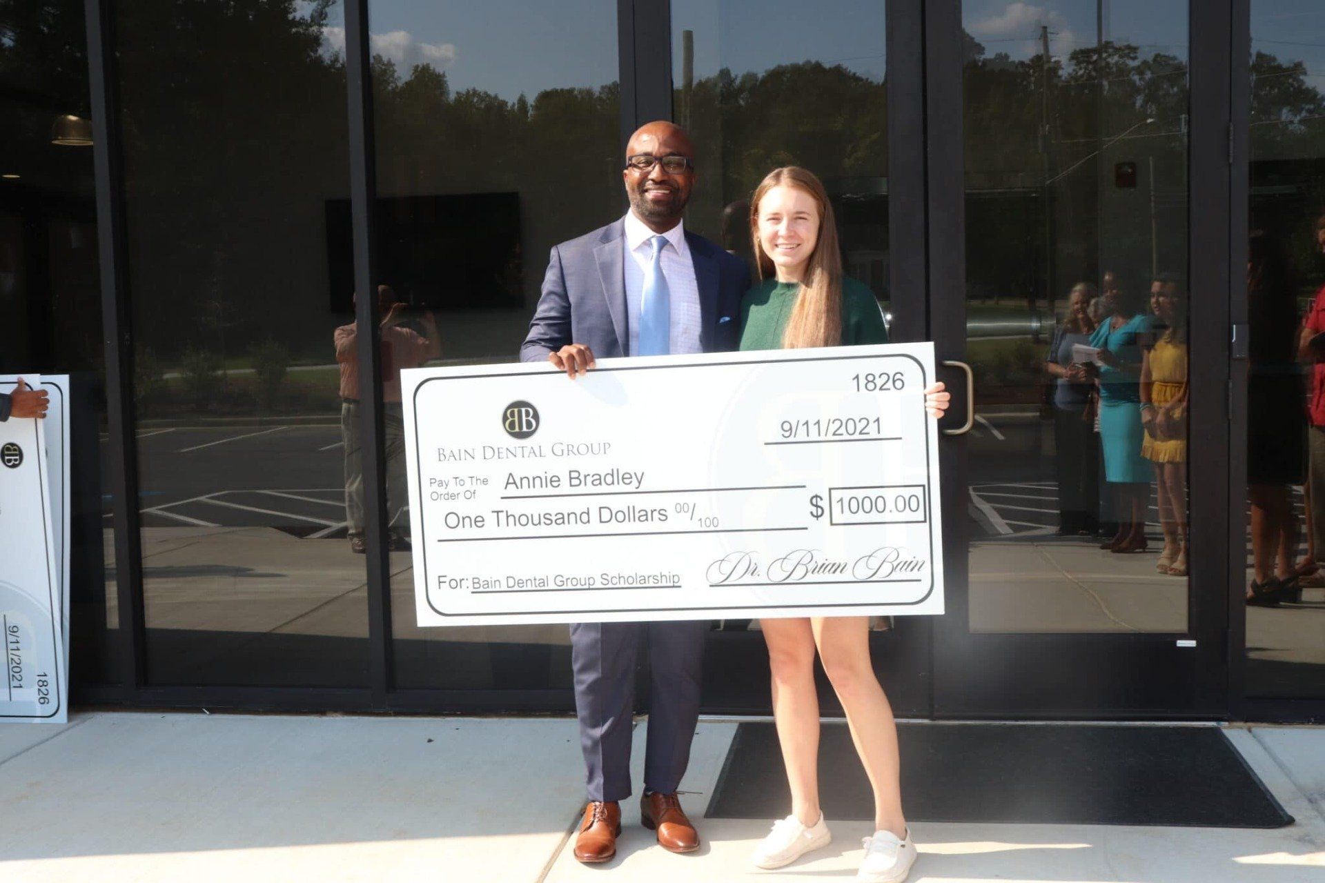 A man and a woman are holding a large check in front of a building.