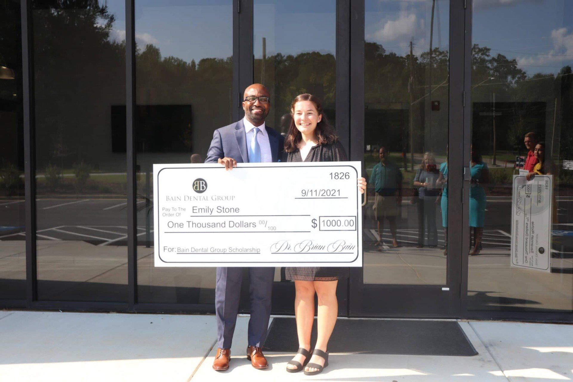 A man and a woman are holding a large check in front of a building.