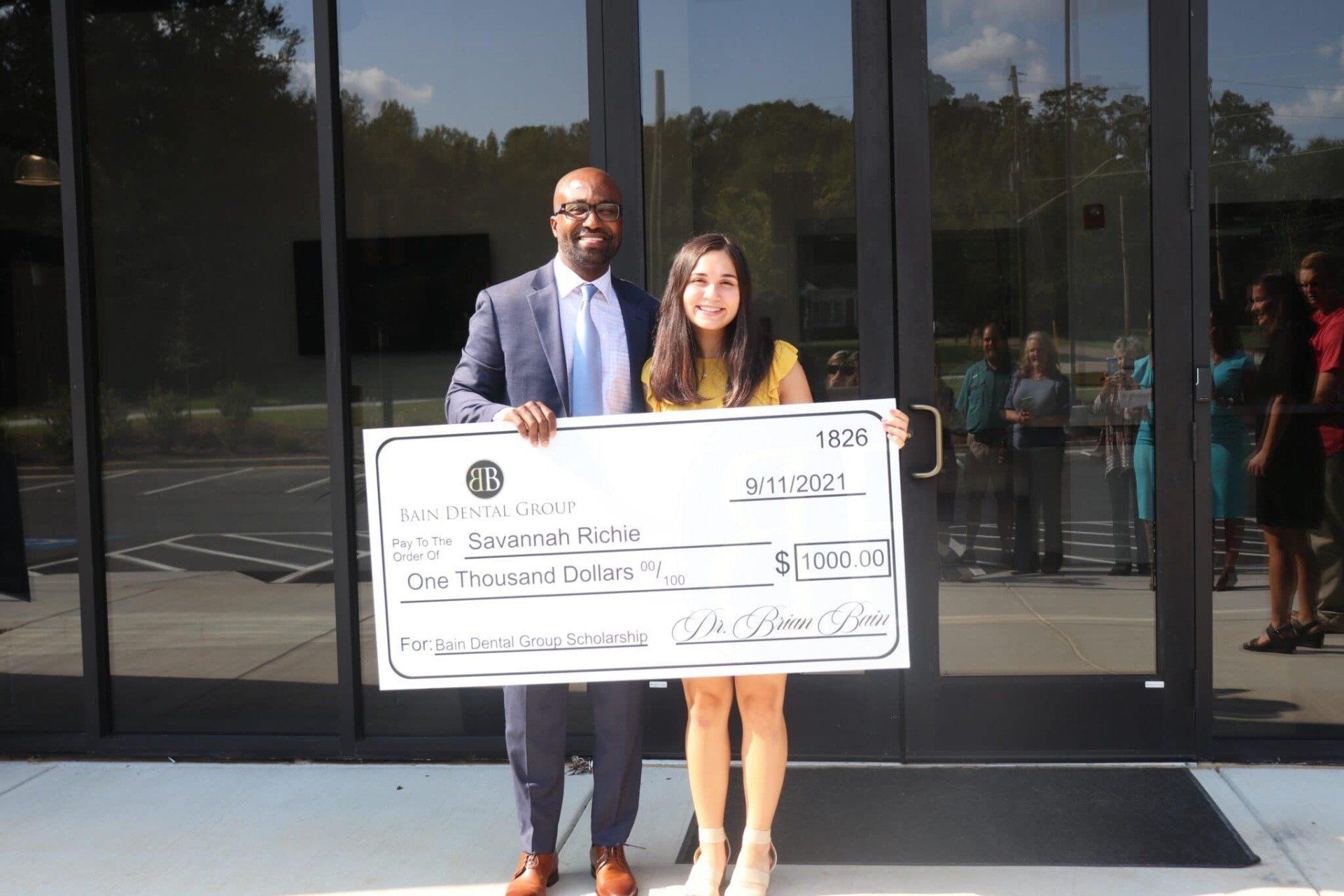 A man and a woman are holding a large check in front of a building.