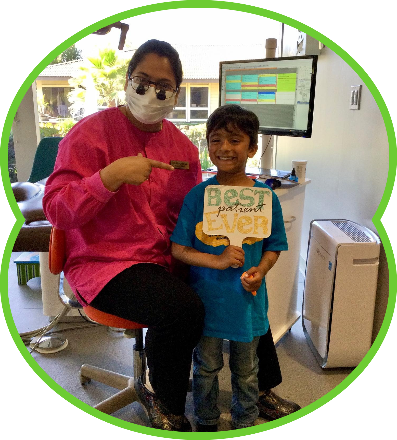 Woman in pink beside smiling child holding a sign in a clinic waiting area