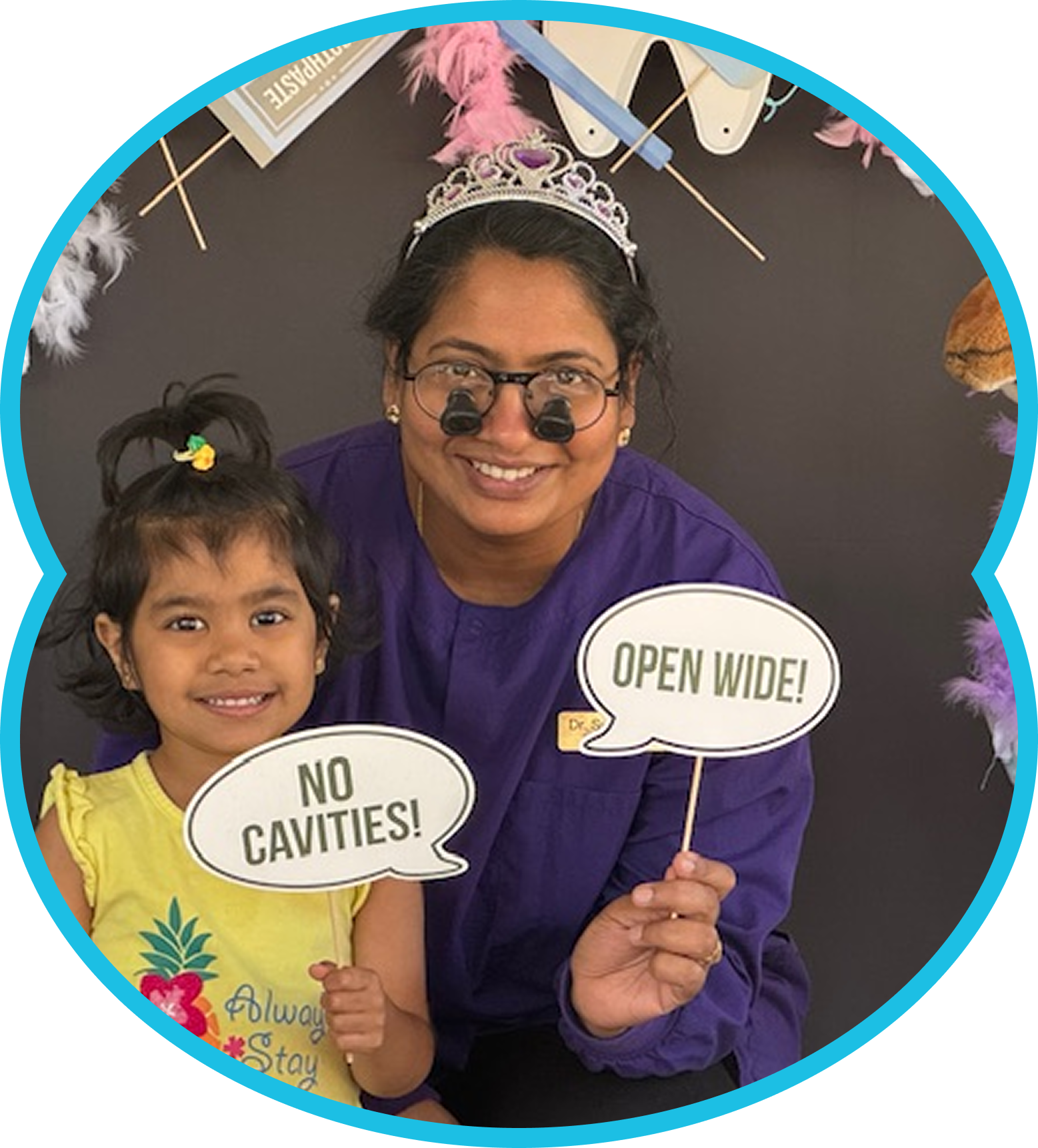 Adult and child smiling with dental props reading “No Cavities!” and “Open Wide!”