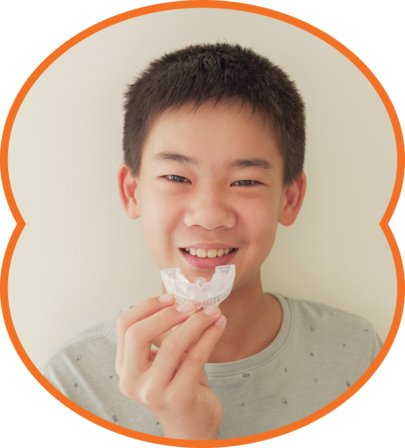 Smiling child holding a clear dental aligner against a white background.