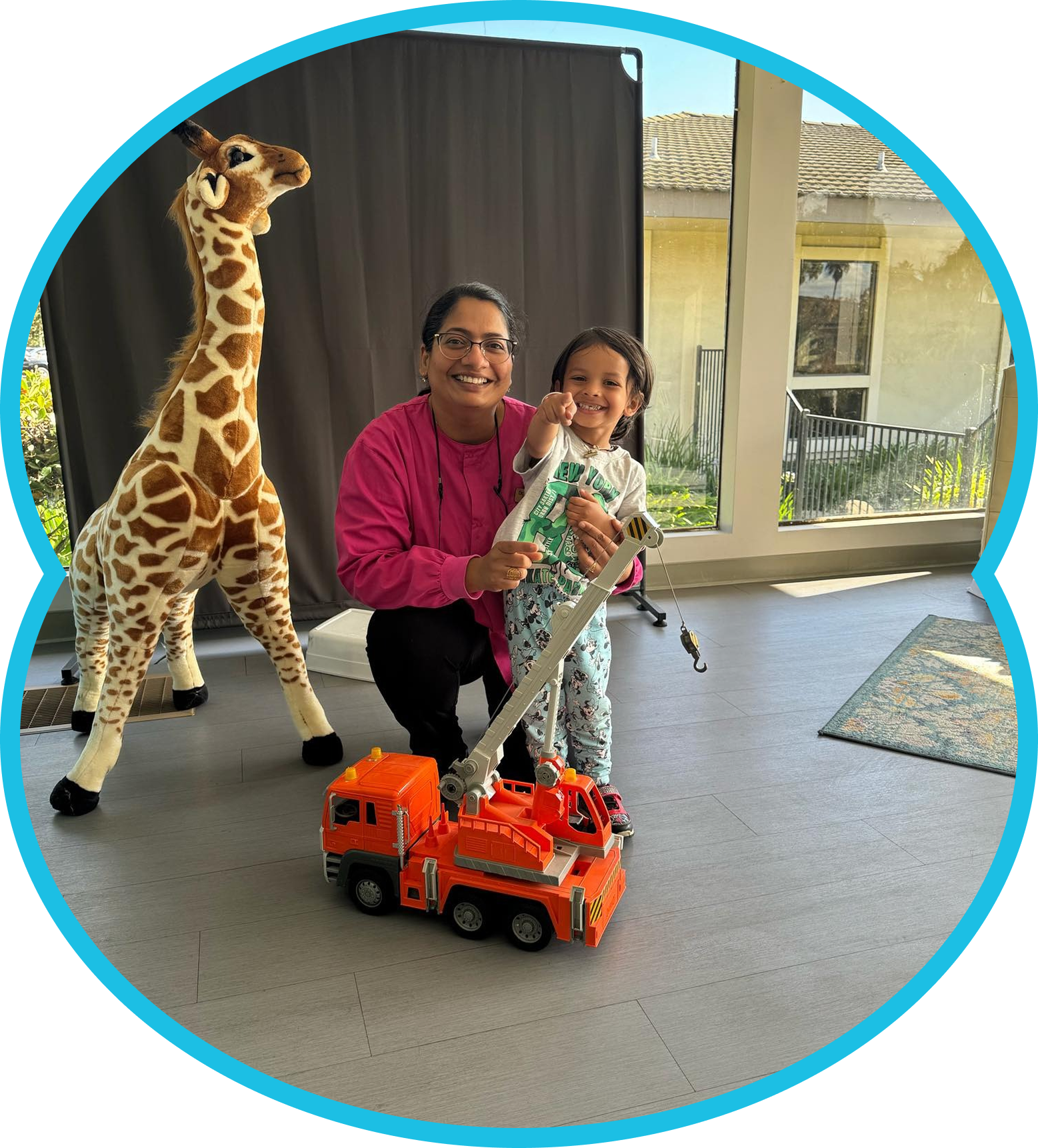Smiling adult and child pose indoors with a toy truck and giraffe figure near a window.