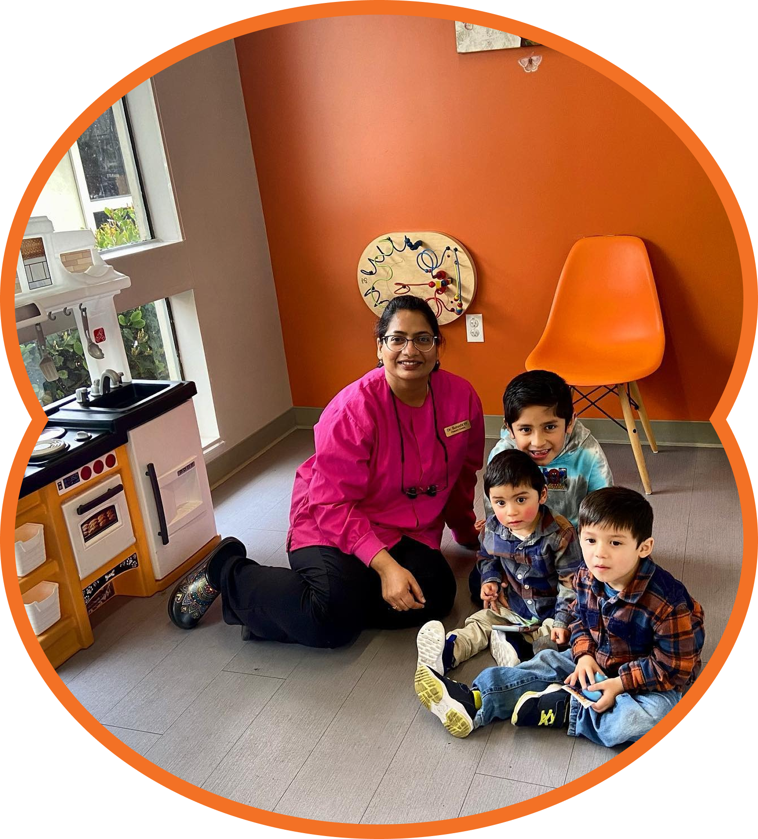 Woman in pink sits with three children in a colorful classroom corner.
