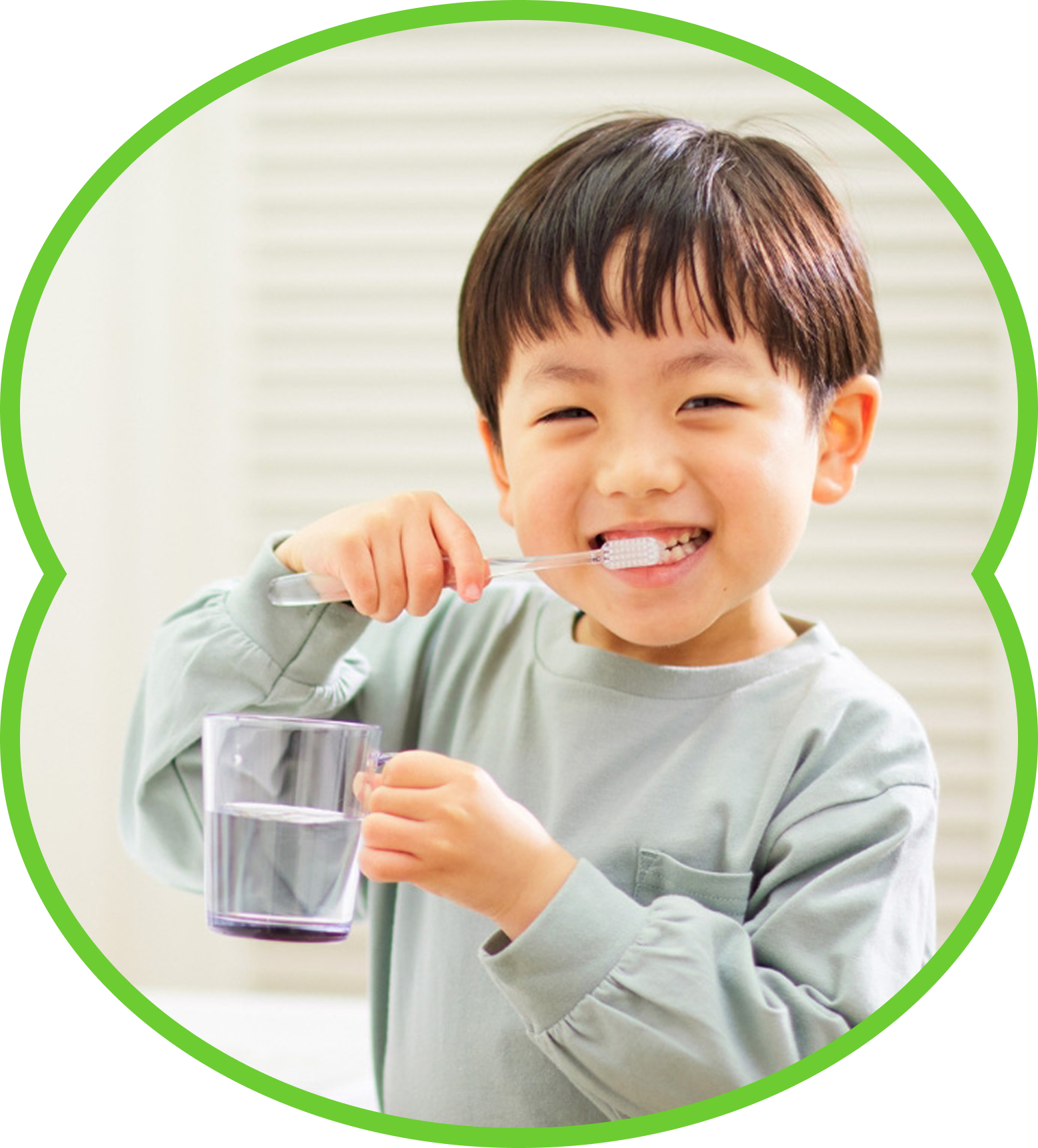 Child brushing teeth while holding a cup of water, smiling in a bright bathroom.
