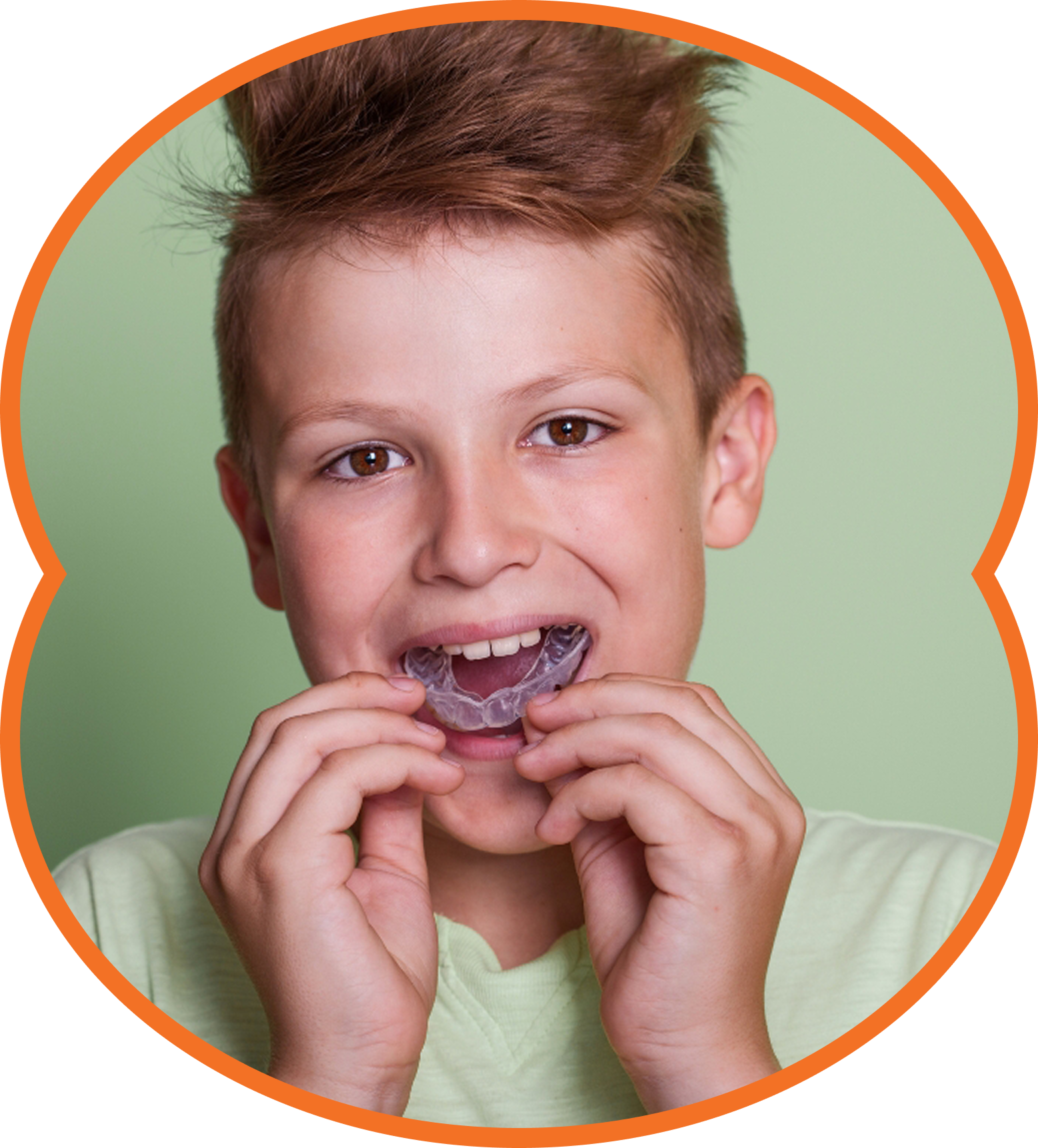 Boy holding and fitting a clear dental retainer in his mouth against a green background.
