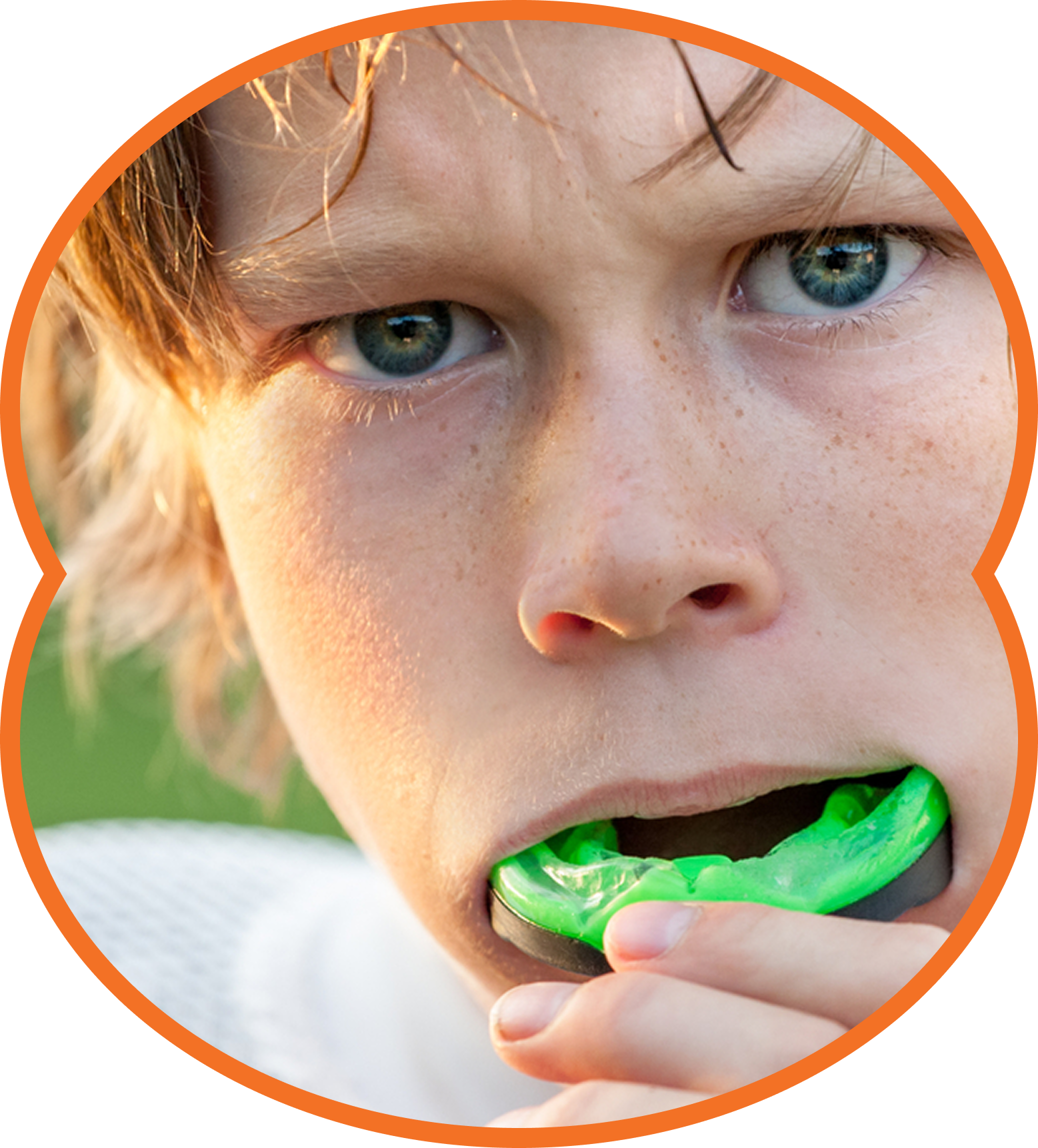 Close-up of a child biting a bright green mouthguard, with a focused expression in warm sunlight