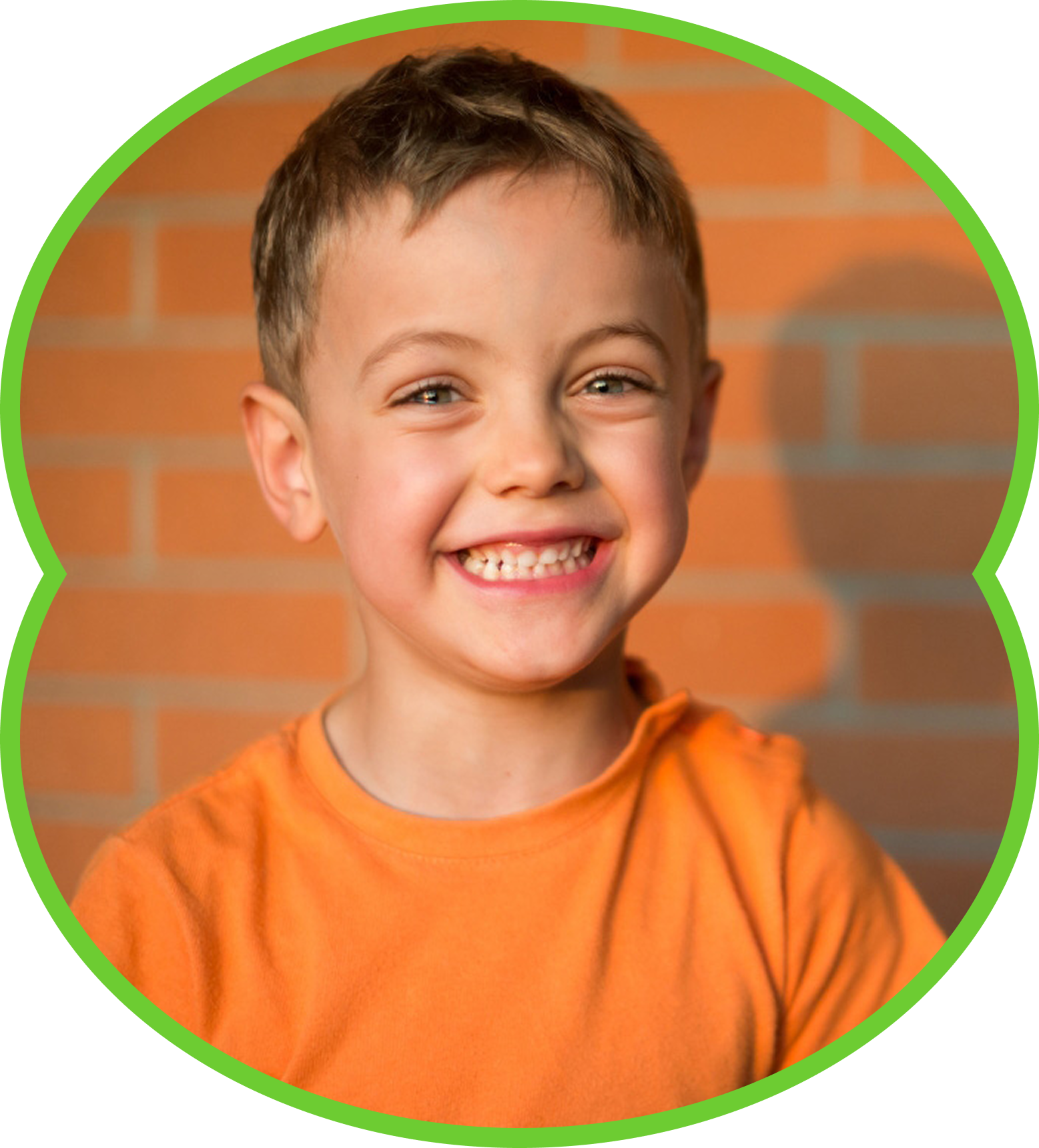 Smiling child in an orange shirt against a brick wall, framed by a green circular border