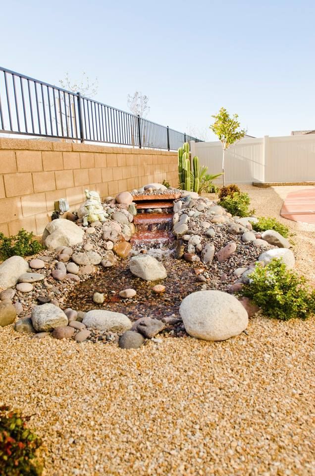 Water feature in a landscaped backyard with a small waterfall, rocks, and gravel ground cover.