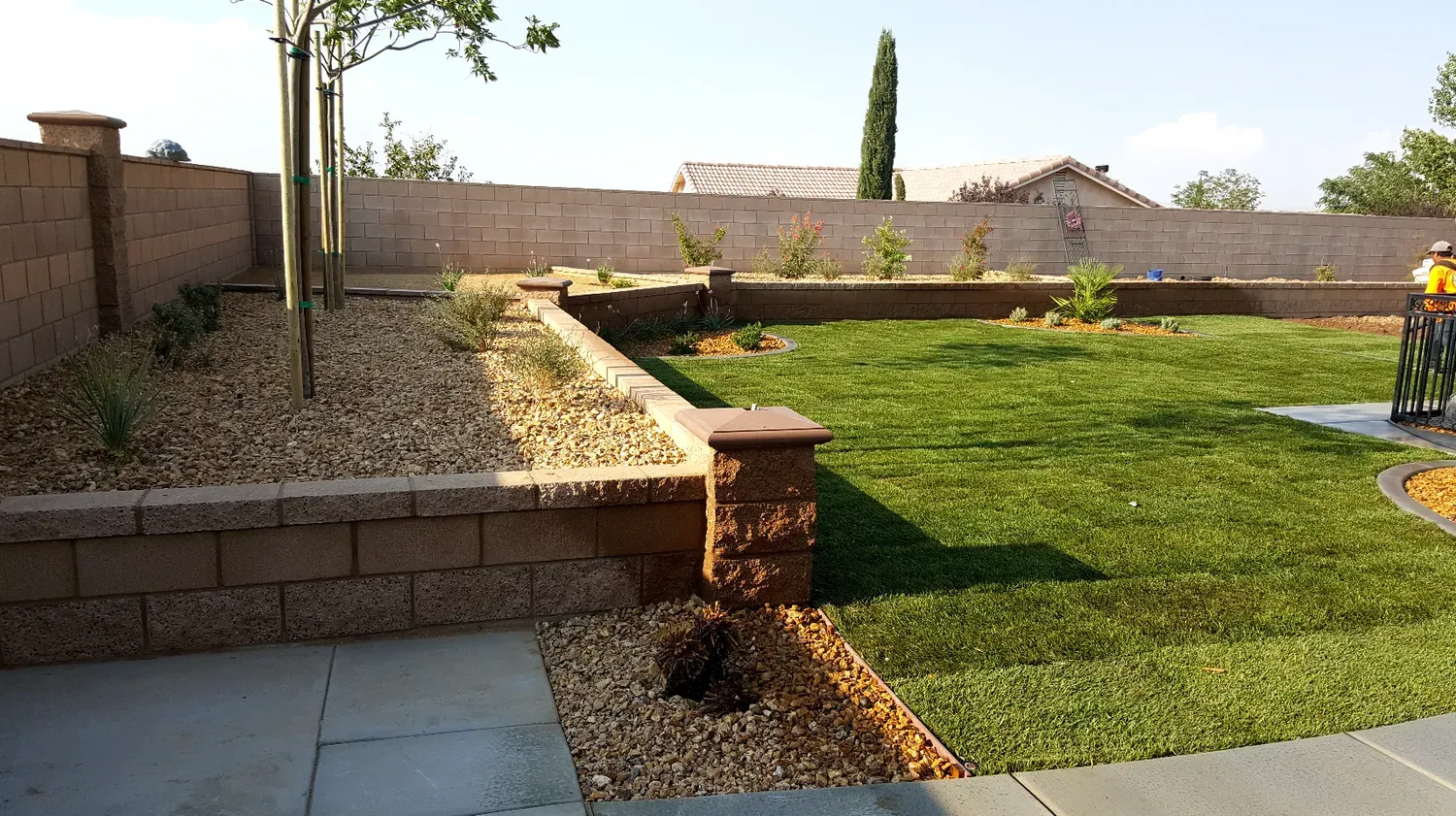 Backyard with raised brick beds, gravel, and a green lawn.