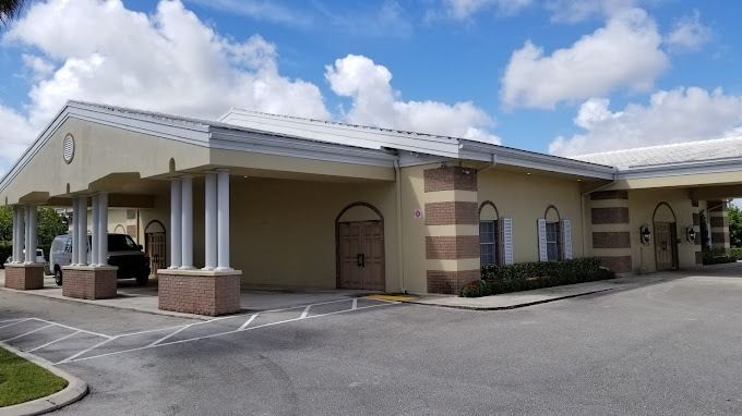 Exterior view of a beige building with a flat roof and columns, with covered drop-off areas.