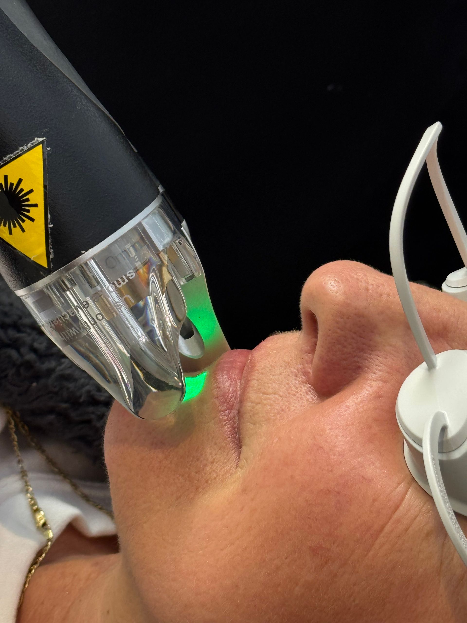 Person wearing a transparent medical mask with green lights on the face, lying on a treatment table