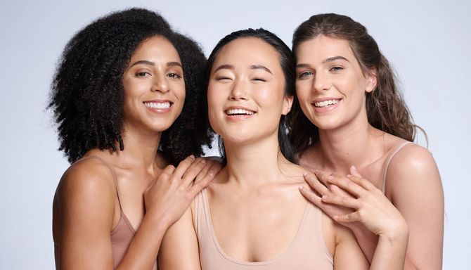 Three smiling people in light tops pose closely against a pale background.