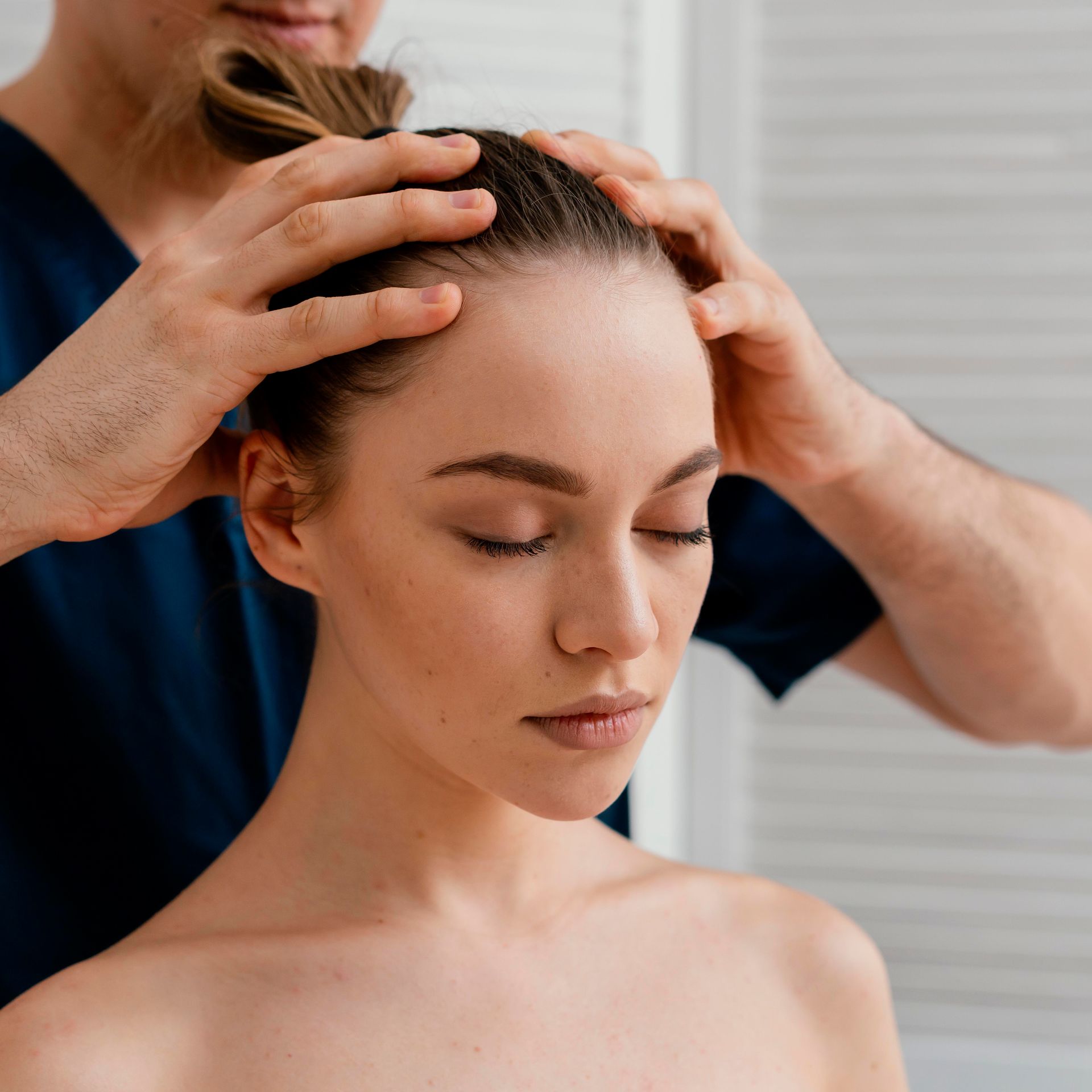 Hands massaging a woman’s scalp with eyes closed in a spa setting