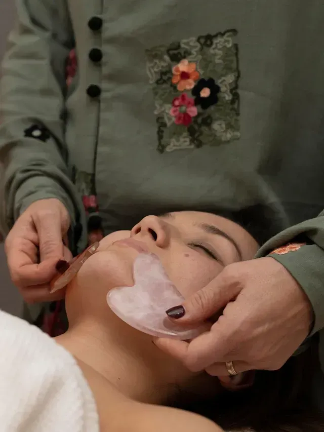 Person applying a facial treatment to a reclining client with a pink gauze mask under the chin