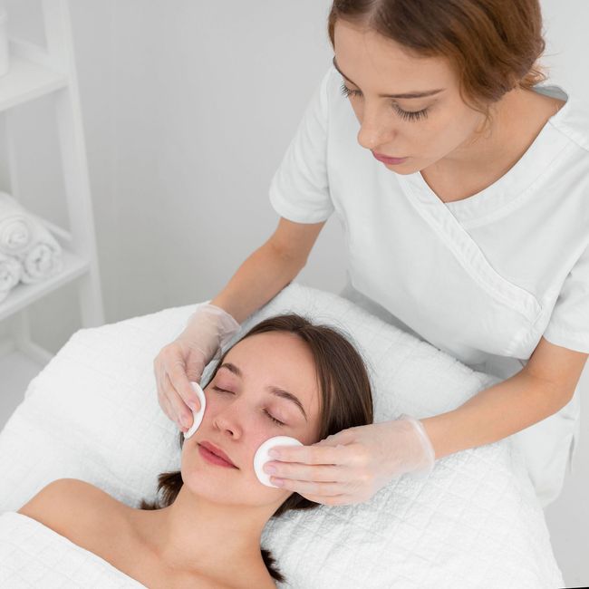Facial treatment with a beautician applying cotton pads to a client’s face on a spa bed