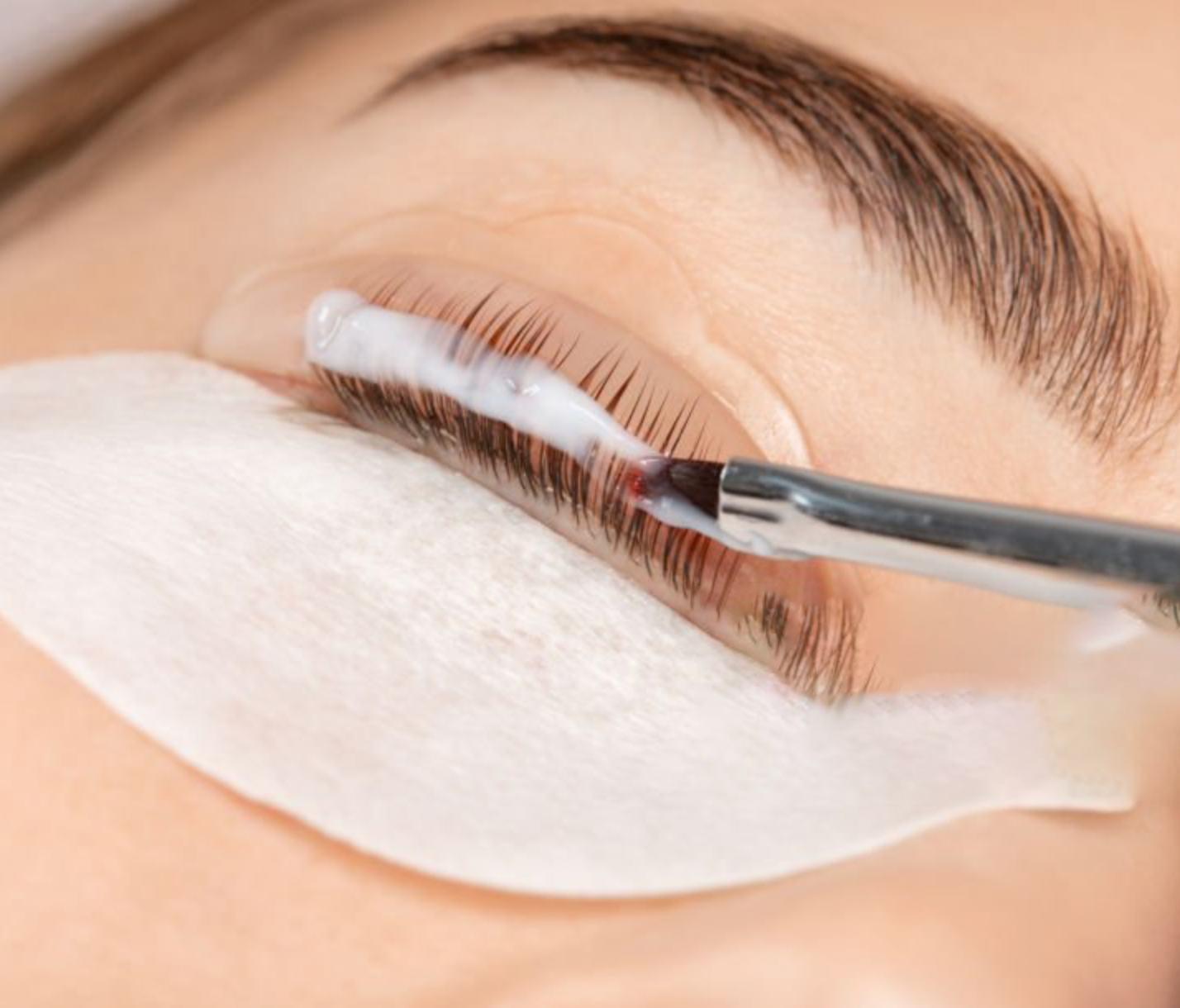 Close-up of eyelash extension application with white under-eye pad and tweezer tool