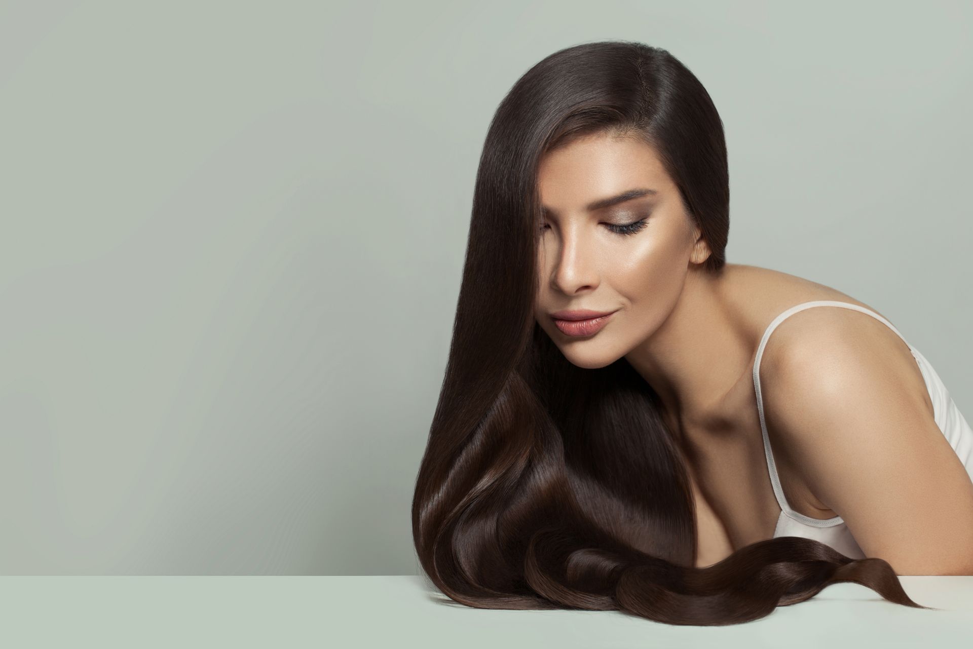 Woman with long dark hair leaning forward against a light gray background